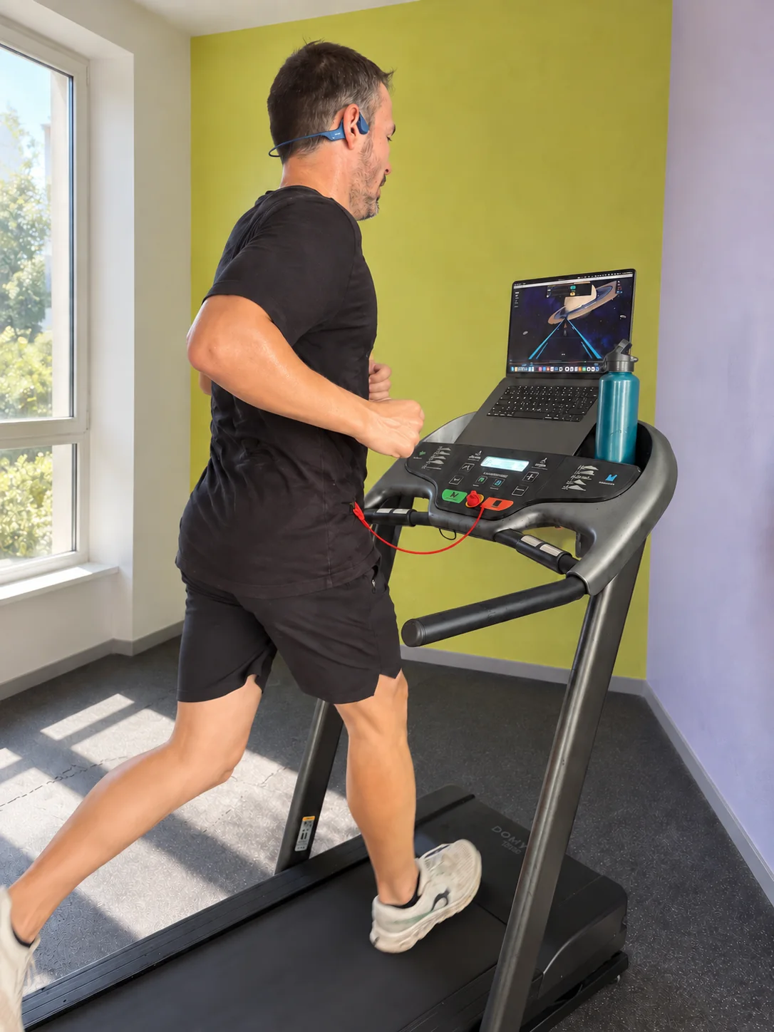 A runner mid-stride on a treadmill in a bright room with green and lilac walls.